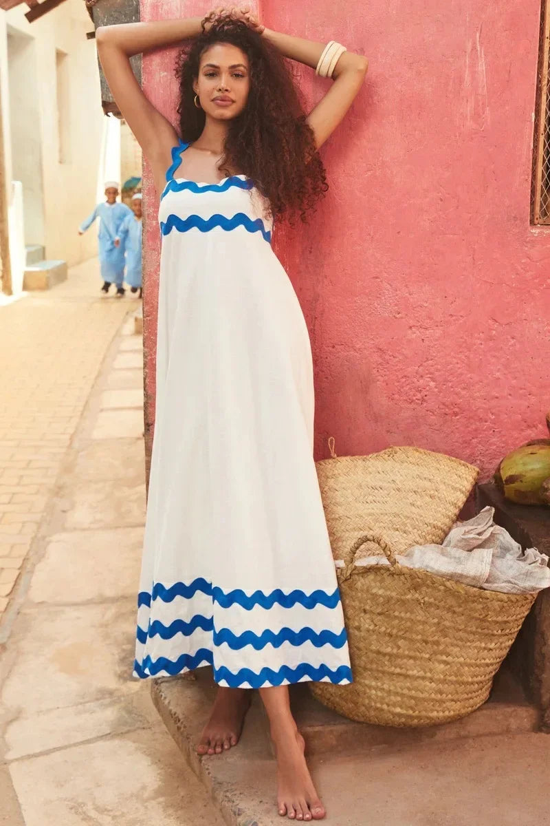 Woman in a white dress with blue stripes standing against a pink wall.