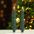Two green tree-shaped candles with a festive background featuring blurred lights and a Christmas tree.