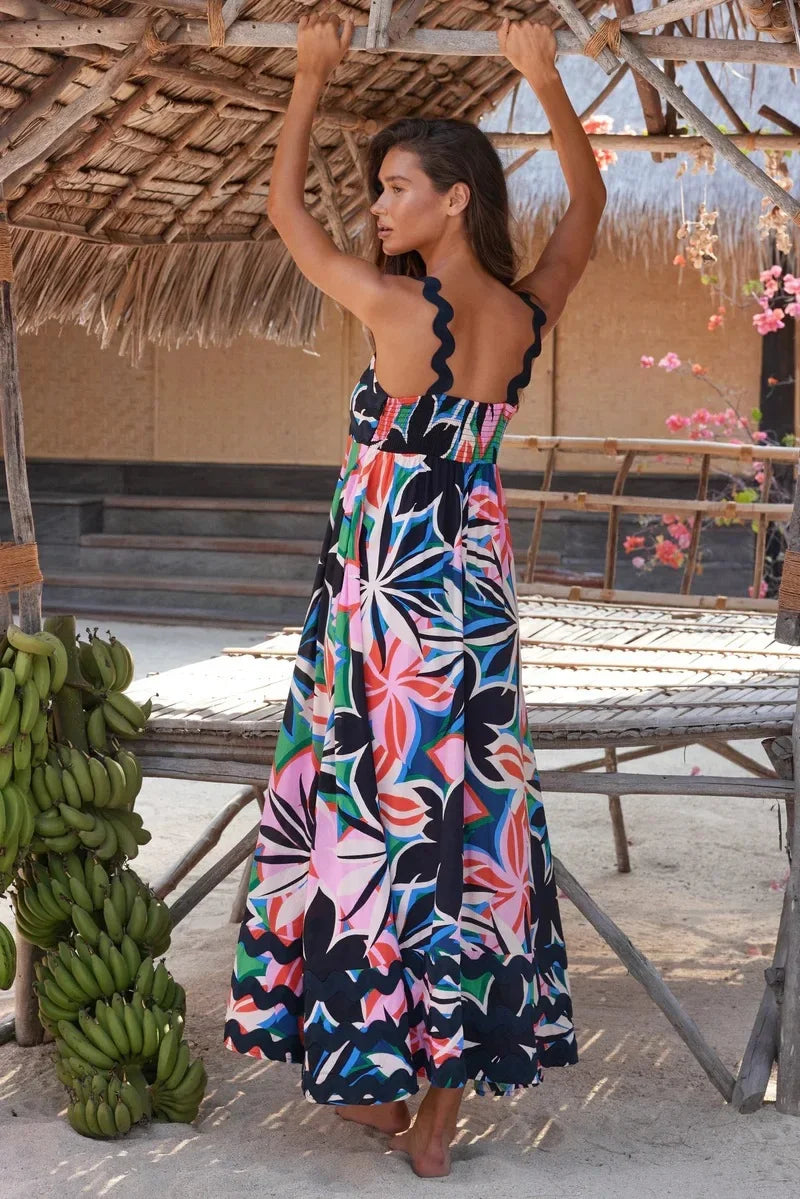 Woman in a colorful floral dress standing under a thatched roof with bananas and flowers in the background.